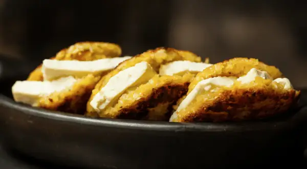 Arepas de choclo doradas y crujientes, rellenas de queso blanco fresco, servidas en un cuenco de barro.