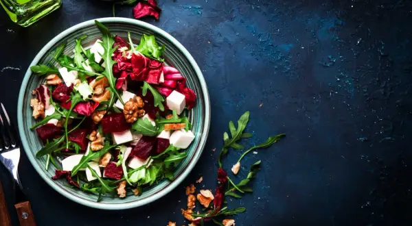 Ensalada de remolacha vibrante con queso feta, nueces y rúcula en un plato azul.