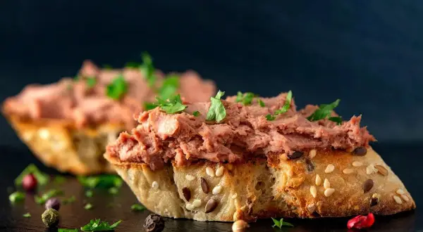Rebanadas de pan rústico con un generoso untado de paté de hígado de pollo, decorado con perejil fresco y granos de pimienta.