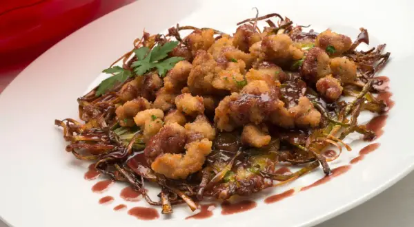 Mollejas de cordero rebozadas y crujientes, servidas sobre verduras salteadas y bañadas en una salsa oscura. ¡Una delicia para aprender como hacer mollejas de cordero!