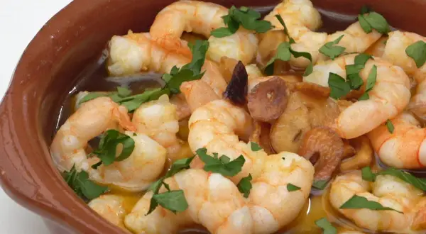 Gambas al pil pil burbujeantes en cazuela de barro, con ajo dorado y perejil fresco.