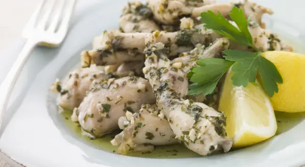 Deliciosas ancas de rana en salsa de ajo y perejil, servidas con gajos de limón. Una receta clásica para disfrutar.