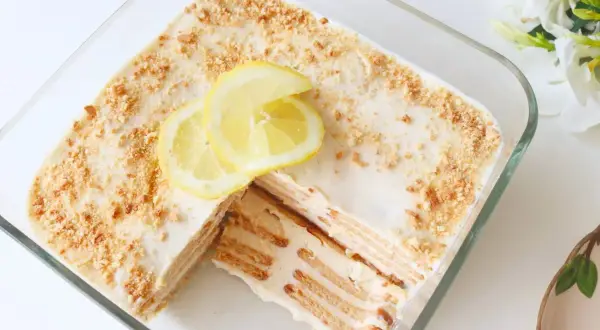 Deliciosa carlota de limón en un recipiente de vidrio, decorada con rodajas de limón y migas de galleta.