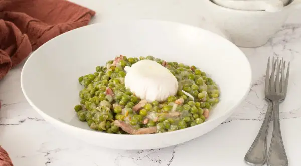Un plato de guisantes a la francesa cremosos con trocitos de panceta y un huevo escalfado encima.
