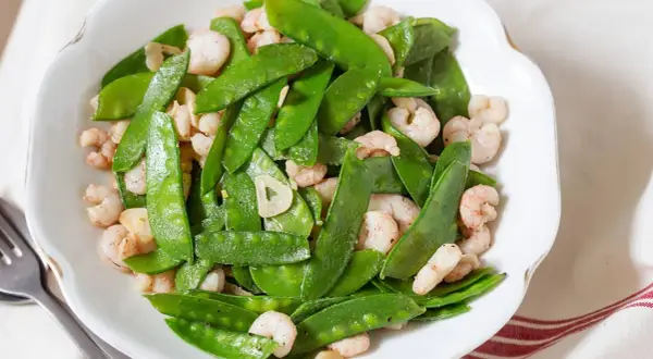 Plato de tirabeques salteados con gambas y ajo. Los tirabeques, crujientes y verdes, se mezclan con las gambas rosadas y láminas de ajo.