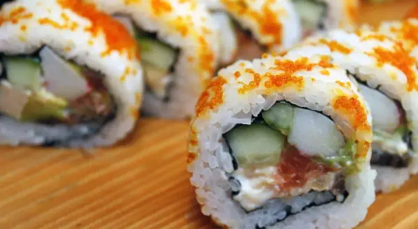 Rollos de sushi caseros con salmón, aguacate y pepino, cubiertos de tobiko. ¡Una guía fácil de como hacer sushi en casa!