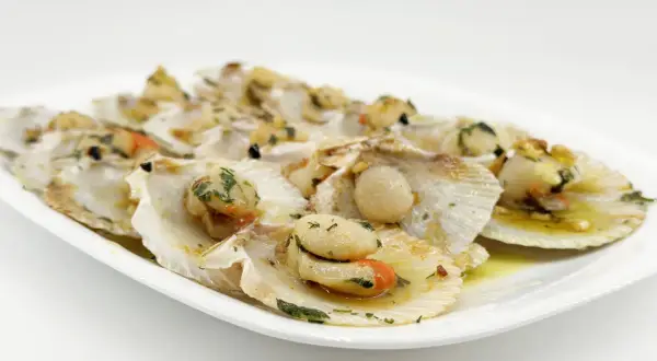 Zamburiñas a la plancha, jugosas y doradas, servidas en su concha con perejil picado y un toque de ajo.