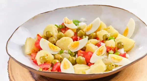 Ensalada campera con patatas, huevos cocidos, tomates y aceitunas verdes, servida en un cuenco rústico.