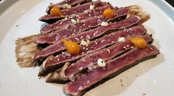 Tataki de ternera, finas lonchas de carne rosada con sésamo, sal gorda y toques de salsa y puré de mango.