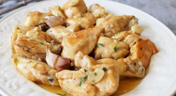 Sabroso pollo al ajillo servido en un plato blanco, con trozos de pollo dorados y jugosos, cubiertos con una salsa de ajo y perejil.