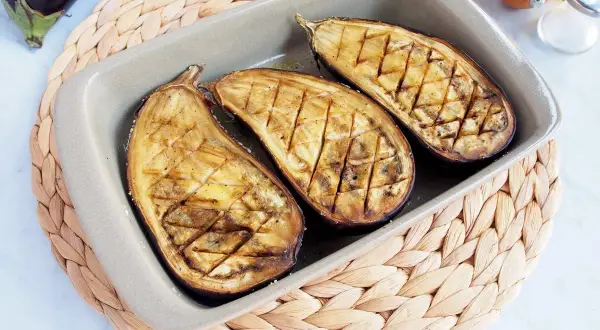 Berenjenas asadas al horno, cortadas por la mitad y con un patrón de rejilla, listas para disfrutar.
