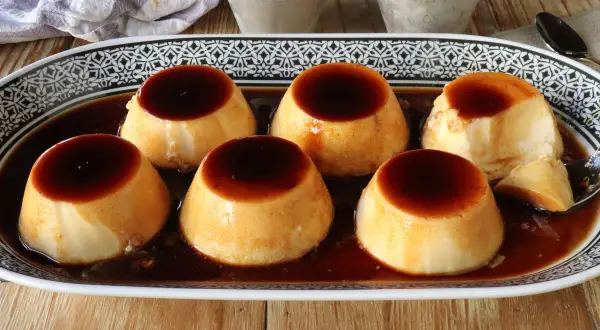 Seis deliciosos flanes de leche condensada, bañados en caramelo oscuro, servidos en una bandeja decorada.