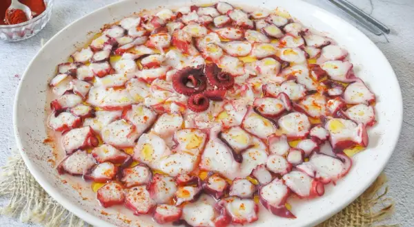 Delicioso carpaccio de pulpo, finas láminas rociadas con aceite de oliva y pimentón, listo para disfrutar.