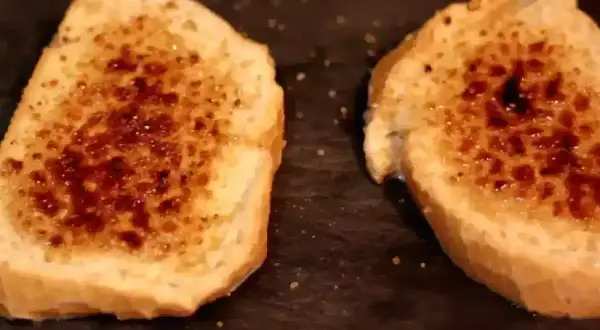 Dos rebanadas de pan tostado con azúcar caramelizada encima, listas para ser horneadas como torrijas.
