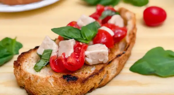 Una bruschetta que es un pan tostado cubierto con tomates frescos, cubos de mozzarella y hojas de albahaca verde.