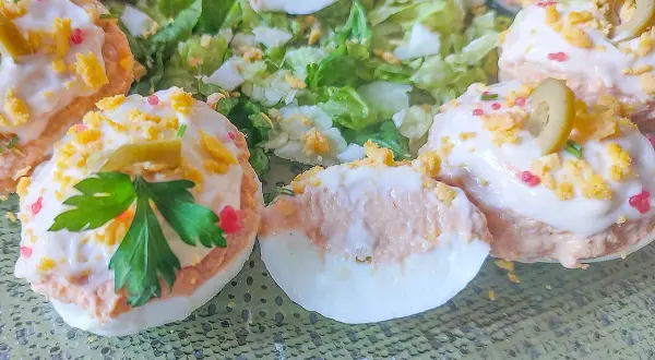 Deliciosos huevos rellenos adornados con aceitunas, perejil y trocitos de huevo duro, servidos sobre una cama de lechuga fresca.