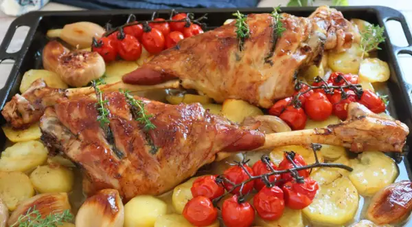 Pierna de cordero al horno jugosa, con patatas, tomates cherry y cebolla. ¡Un festín para los sentidos!
