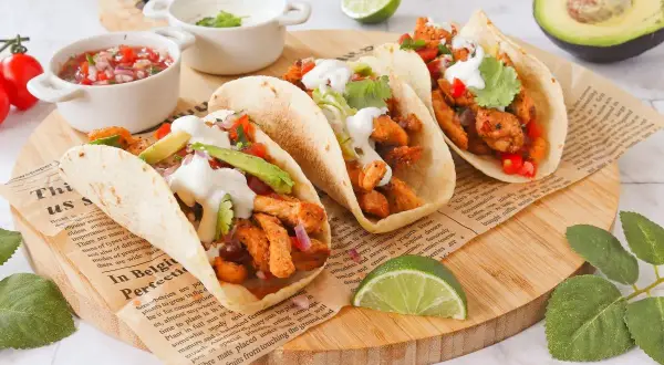 Cuatro deliciosos tacos de pollo con aguacate, cilantro y crema, acompañados de pico de gallo y limón.