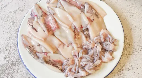 Plato con chipirones limpios y tentáculos listos para freír. Se aprecian sus manchas oscuras y tonos rosados.