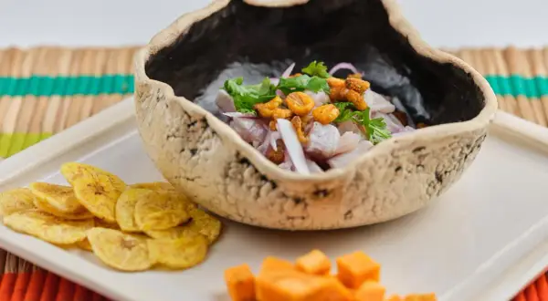 Delicioso ceviche de corvina en cuenco rústico, acompañado de patacones y cubos de camote.