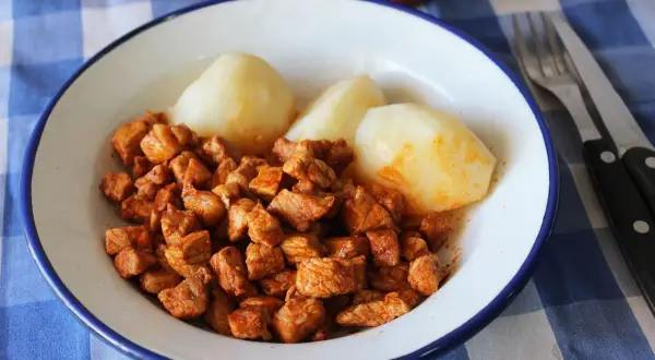 Plato de zorza con patatas, servido en un cuenco blanco con borde azul sobre un mantel de cuadros azules.