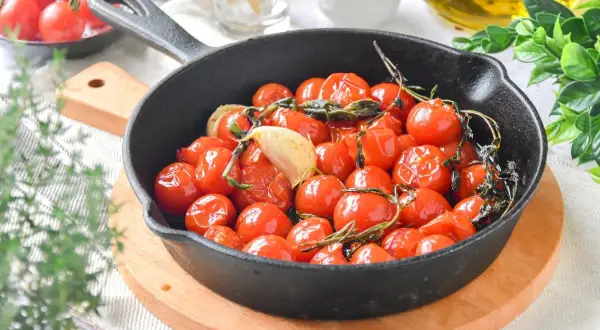 Tomates cherry confitados en sartén de hierro fundido con ajo y hierbas. Un plato delicioso y aromático.
