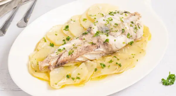 Delicioso rape al horno sobre cama de patatas laminadas, espolvoreado con perejil fresco.