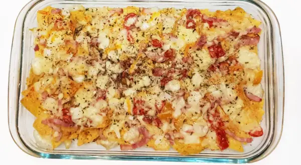 Nachos con queso horneados, cubiertos con trozos de tocino y pimientos rojos.