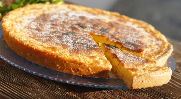 Un delicioso postre típico de Ibiza, una tarta dorada espolvoreada con azúcar glas, con una porción cortada.