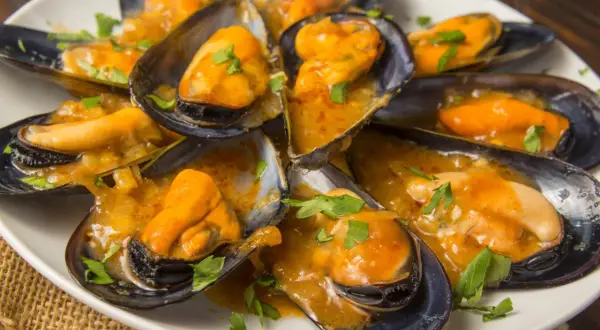 Mejillones en salsa, como los de los bares, servidos en una cazuela blanca con perejil picado.