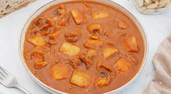 Un plato humeante de jibia en salsa, con trozos de patata y pan rústico al lado.