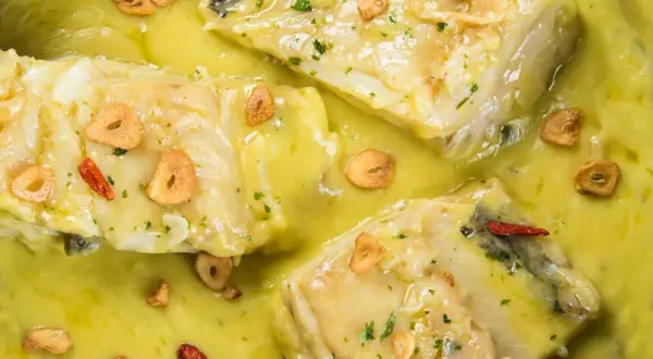 Merluza al pil pil, jugosos trozos de pescado blanco en una salsa cremosa con láminas de ajo crujiente y guindilla.