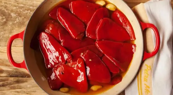 Pimientos del piquillo asados en una cazuela roja, con ajos y un paño de cocina.