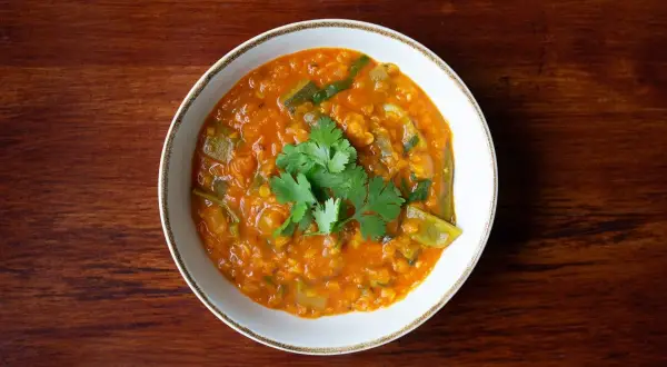 Un tazón de lentejas al curry, con cilantro fresco, servido sobre una mesa de madera.