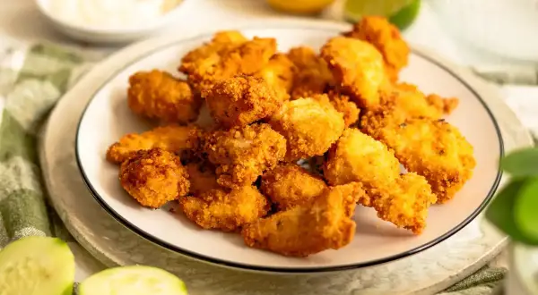 Plato de lagrimitas de pollo crujientes, acompañadas de rodajas de pepino y limón.