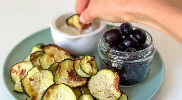 Crujientes rodajas de calabacín en airfryer, servidas con aceitunas negras y una salsa para mojar.