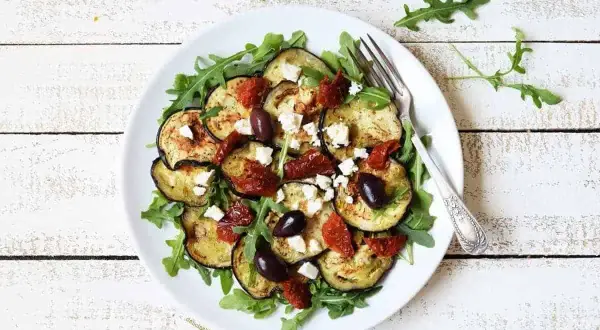 Deliciosa ensalada de berenjena asada con rúcula, tomates secos, aceitunas negras y queso feta.