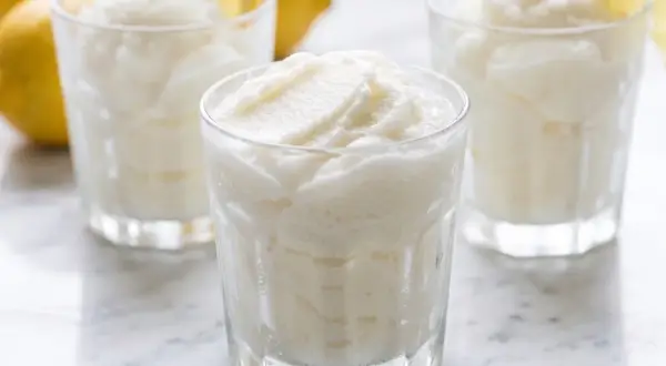 Tres vasos de sorbete de limón, refrescante y cremoso, con limones amarillos y hojas de menta al fondo.