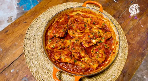 Pollo a la toledana en cazuela naranja, servido sobre una esterilla de mimbre en una mesa de madera rústica.
