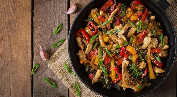 Wok de pollo con pimientos de colores y judías verdes, espolvoreado con sésamo y cebolleta.