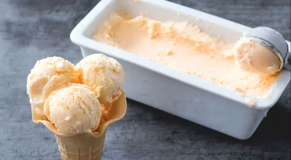 Un cono con tres bolas de helado de melón cremoso y una cubeta llena de este refrescante postre.