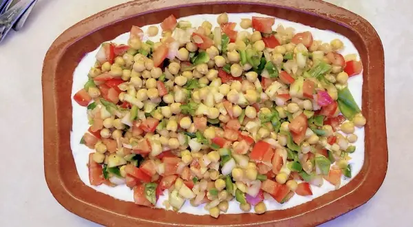 Deliciosa ensalada de garbanzos con tomate, pimiento y cebolla, servida sobre una base cremosa en un cuenco de barro.