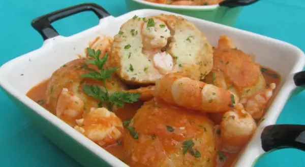 Albondigas de rape con gambas en salsa, servidas en cazuelas verdes y blancas, decoradas con perejil fresco.