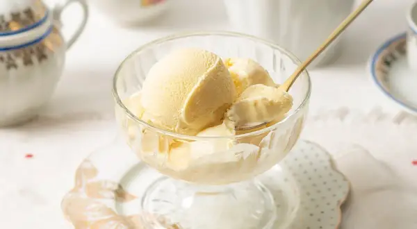 Copa de cristal con cremoso helado de mantecado, lista para disfrutar. Una cuchara dorada toma una porción.