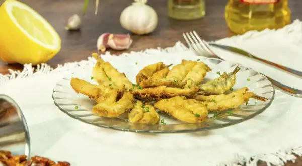 Un plato de boquerones en adobo crujientes, servidos con limón, ajo y guindillas.