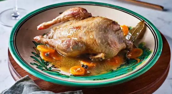 Perdiz a la toledana servida en plato decorado con rodajas de zanahoria y especias.