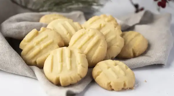 Montón de galletas de mantequilla doradas con líneas marcadas, servidas sobre una tela gris.
