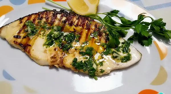 Delicioso emperador a la plancha con perejil fresco, ajo y limón, servido en un plato blanco con círculos de colores.