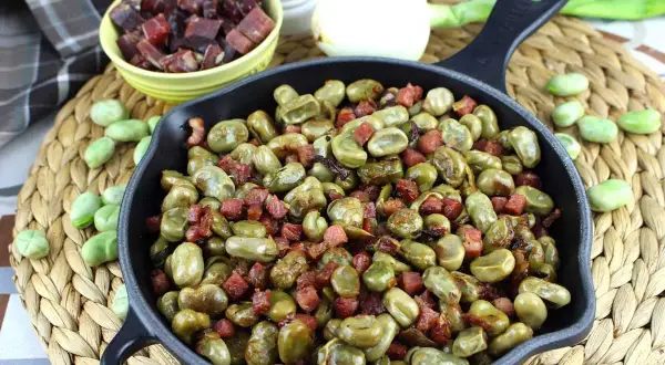 Habas tiernas salteadas con trocitos de jamón en una sartén de hierro fundido, un plato tradicional lleno de sabor.