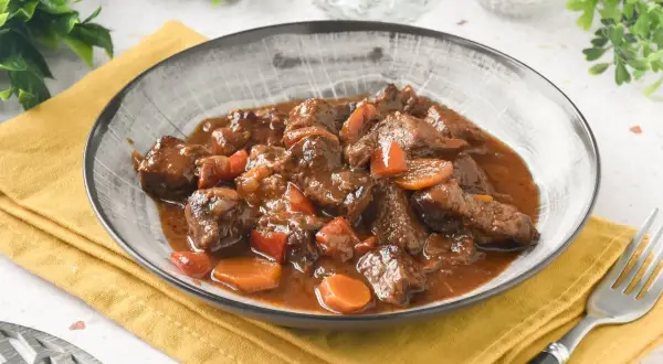 Un plato humeante de carne al toro, tierno y jugoso, con trozos de zanahoria y pimiento en una rica salsa.